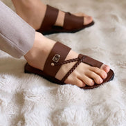 les sandales KIATEMA en cuir marron sont portées par un modèle, illustrant leur ajustement confortable et leur style élégant. La sangle tressée et la finition en cuir haut de gamme sont mises en valeur, démontrant l'artisanat sénégalais.