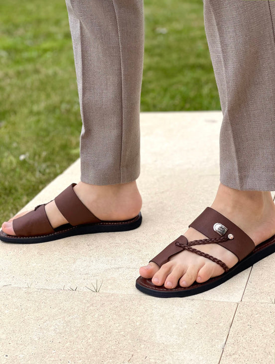les sandales KIATEMA en cuir marron sont portées par un modèle, illustrant leur ajustement confortable et leur style élégant. La sangle tressée et la finition en cuir haut de gamme sont mises en valeur, démontrant l'artisanat sénégalais.