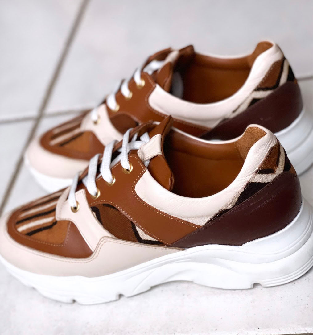 Caractéristiques: * Tige: En cuir véritable et tissu bogolan * Semelle intérieure: Confort orthopédique * Semelle extérieure: Caoutchouc robuste pour une adhérence optimale * Fermeture: Lacets en coton renforcé * Couleur: Mélange de blanc, beige et marron * Taille disponible: Du 36 au 45 Avantages: * Confort: Conception ergonomique pour un usage quotidien * Durabilité: Matériaux de haute qualité pour une longue durée de vie * Style: Design contemporain avec une touche culturelle unique * Polyvalence: Idéale