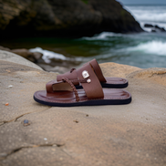 les sandales KIATEMA en cuir marron sont portées par un modèle, illustrant leur ajustement confortable et leur style élégant. La sangle tressée et la finition en cuir haut de gamme sont mises en valeur, démontrant l'artisanat sénégalais.